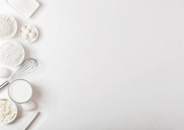 Beyaz masa arka planında taze süt ürünleri. Bir bardak süt, bir kase un, ekşi krema ve süzme peynir ve yumurta. Çelik çırpıcı