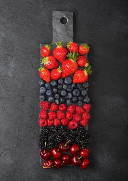 Fresh organic summer berries mix on black marble board on dark kitchen table background. Raspberries, strawberries, blueberries, blackberries and cherries. Top view