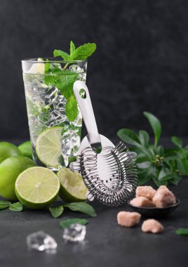 Bir bardak buzlu mojito kokteyli, siyah tahtada naneli ve limonlu süzgeç ve kamış şekerli taze limon. En iyi parti içkisi.