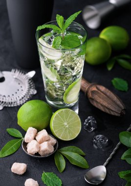 Bir bardak naneli mojito kokteyli ve siyah tahta üzerinde limon kaşık ve taze limon ve kamış şekeri tahta sıkacağı ve buzlu siyah karıştırıcı. En iyi yaz kokteyli.