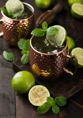 Bakır bardakta Moskova katırı kokteyli, kireç, nane ve ahşap sıkacağı koyu ahşap masa arkasında..