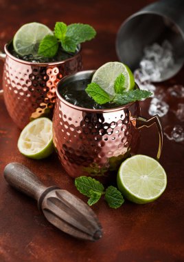 Limonlu ve biberiyeli bakır bardakta Moskova katır kokteyli. Kahverengi mutfak masasında da ahşap sıkacağı var.