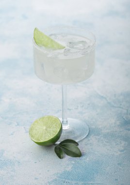 Modern kristal bardak Margarita kokteyli açık mavi masa zemininde taze limon..