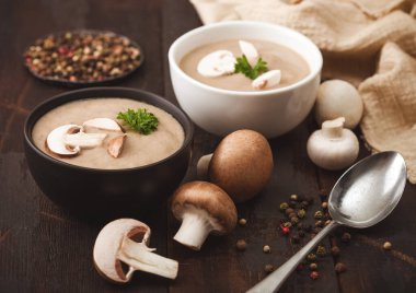 Koyu ahşap tahta üzerinde seramik kase kremalı kestane rengi şampiyon mantar çorbası kaşık, biber ve mutfak örtüsü..