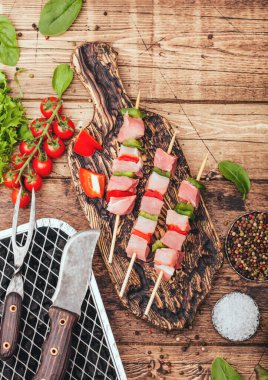 Çiğ domuz kebabı, kırmızı biber ve taze sebzelerle doğranmış tahta kaplama, çatal ve bıçakla tek kullanımlık kömür ızgarası. Marul ve kırmızı biberli tuz..