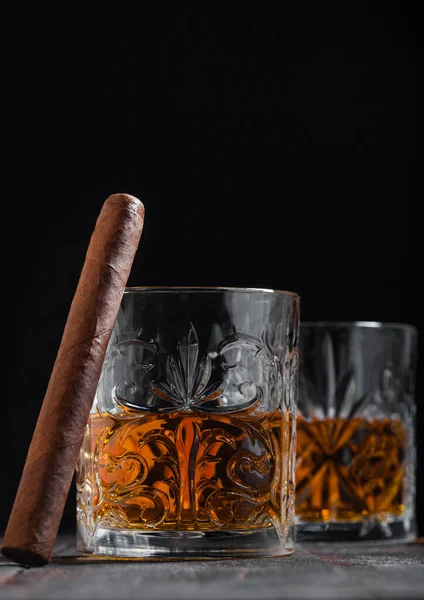 Single malt scotch whiskey in crystal glasses with cuban cigar on wooden table background.