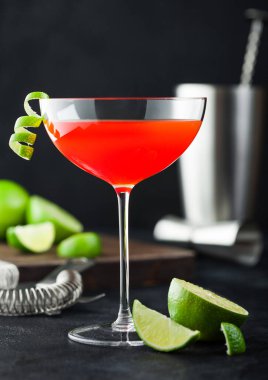 Lüks kristal bardakta kozmopolitan kokteyli, limon kabuğu, süzgeç, jigger ve sallanan taze limonlu siyah masa arkaplanı..