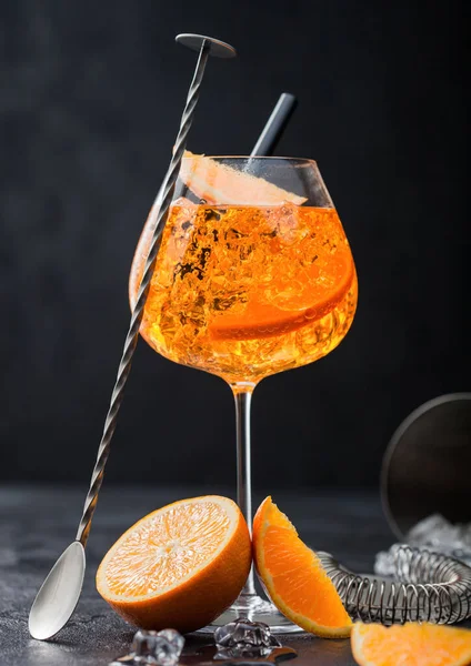 オレンジ色のスライスと黒を基調としたカクテルシェーカー付きのバースプーンを備えたアパールスプリッツ夏のカクテルのグラス 氷のキューブと黒藁 — ストック写真