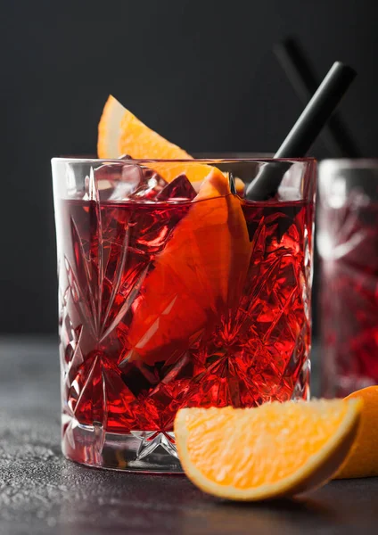 Kristal bardaklarda portakal dilimli Negroni kokteyli ve siyah masa arkaplanlı siyah pipet. Makro