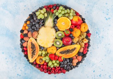 Taze çiğ organik yaz meyveleri ve egzotik meyveler mavi mutfak arka planında büyük tepside. Papaya, üzüm, nektarin, portakal, ahududu, kivi, çilek, liçi, kiraz. Üst görünüm