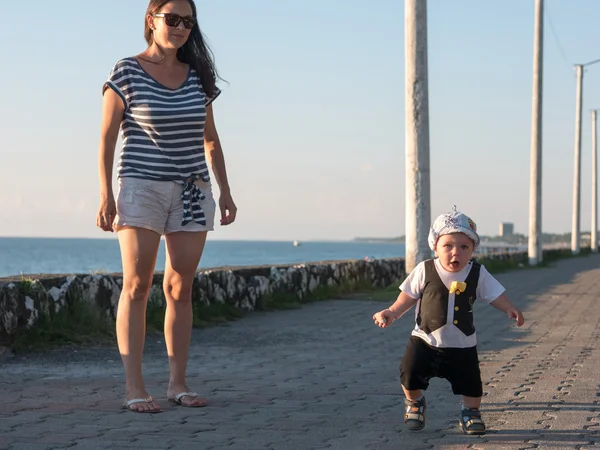 Mãe e filho brincando perto do oceano ao pôr-do-sol. Em um bebê muito bonito expressão facial engraçada — Fotografia de Stock