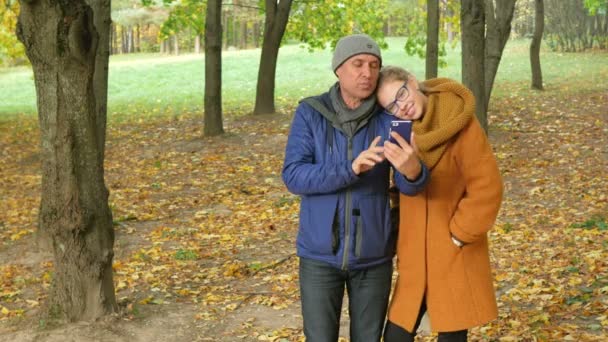 Dochter en vader praten aan de telefoon bij het herfst park op de video. Papa lacht en lacht met haar dochter een tiener. gelukkige familie concept — Stockvideo