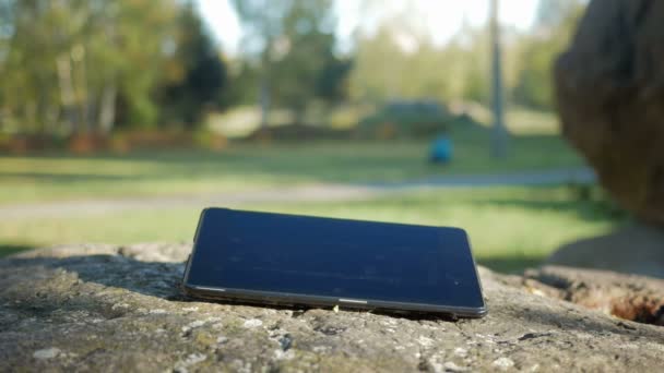 Tablet PC-computer deel uitmaakt van een grote steen in de straat. Mans hand in een groen jasje raakt de plaat. Bewegen van de camera. — Stockvideo