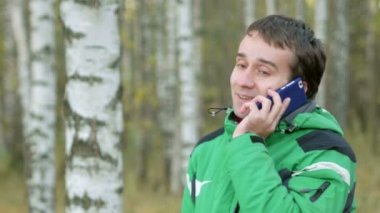 Sonbahar Park cep telefonuyla konuşan adam. Cihazın dokunduktan sonra. Yeşil sıcak spor ceket genç erkeklerde