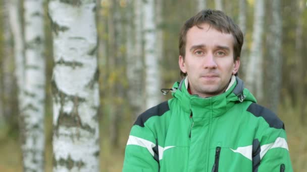 Mladý pohledný muž díval do kamery v podzimním parku. Vybavit zelený Sportovní bunda teplá — Stock video