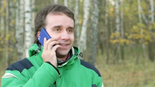 Hombre hablando por celular en el parque otoñal. Después de tocar el dispositivo. Chaqueta deportiva verde cálida en hombres jóvenes — Vídeos de Stock