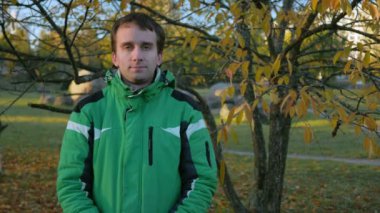 Sonbahar park kamerada bakarak yakışıklı delikanlı. Bir yeşil Spor ceket sıcak donatmak