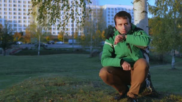 Bir adam akıllı saatler sonbahar parkta sosyal ağlarda iletilerde günbatımında denetler. Sesli yanıt belirler. Yeşil spor ceket ve özenli çalışma cihazın — Stok video