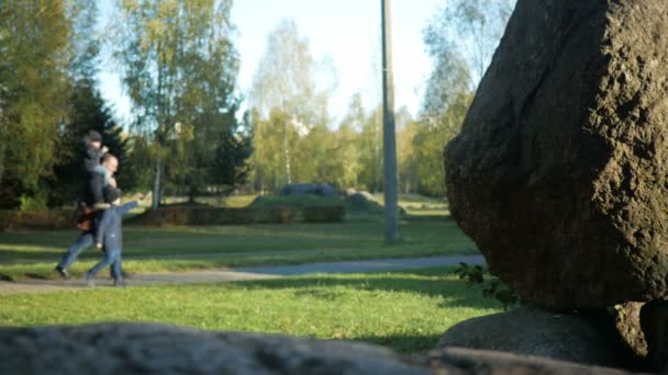 Blurred Background: the father and two sons walking in the park of large stones. A kid sitting on the Popes neck. Autumn time — Stock Video