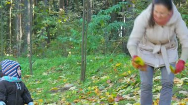 Güzel bebek annesi hakkında düşen yapraklar ile sonbahar parkta oynuyor. Çocuk sıcak bir çanta ve şapkası ile bir eşarp, çocuk yaklaşık bir yıl içinde giyinmiş