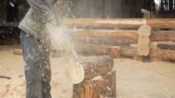 Строитель управляет деревянной бензопилой. На заднем плане - часть будущего дома из деревянных балок, замедленная съемка — стоковое видео