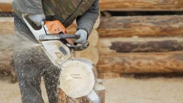Строитель управляет деревянной бензопилой. На заднем плане - часть будущего дома из деревянных балок, замедленная съемка — стоковое видео