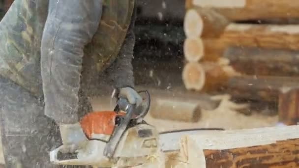 Builder handles wooden timber chainsaw. Against the background is part of the future of the house made of wooden beams, slow motion — Stock Video