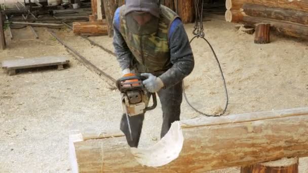 L'uomo fa ricci taglio del legno motosega. Il tronco farà parte del futuro della casa in legno. Maschera protettiva sul viso del costruttore e un sacco di segatura . — Video Stock