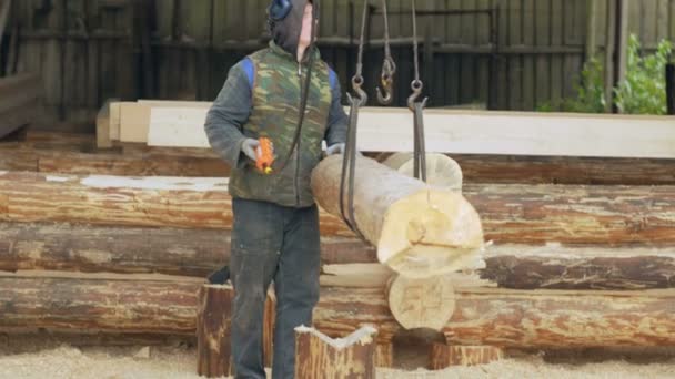 Строитель поднимает деревянную древесину с помощью подъемного крана. Человек держит бревно и переносит его в будущий дом — стоковое видео