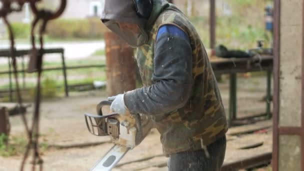 Человек делает кудрявую резку древесины бензопилой. Древесина будет частью будущего деревянного дома. Защитная маска на лице строителя и много опилок . — стоковое видео