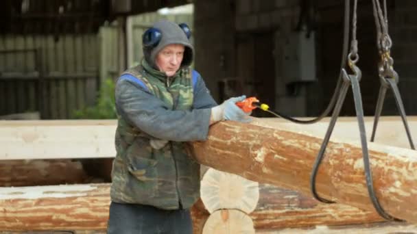 Bouwer verhoogt houten hout met Overhead Lier kraan. Een man houdt een logboek en het overbrengen van de toekomstige woning — Stockvideo