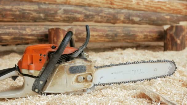 Chainsaw builder at the site of construction of a wooden house. Many sawdust and a part of the future of the house in the background. Close-up and moving camera — Stock Video