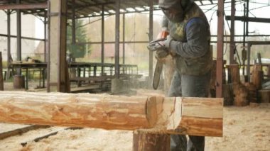 Adam ahşap testere gelecekteki ev için keser. Builder ve bir sürü talaş yüzünde koruyucu yüz maskesi. Hangar gelecekteki ev arka planda bir bölümüyle