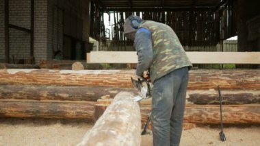 Adam ahşap testere gelecekteki ev için keser. Builder ve bir sürü talaş yüzünde koruyucu yüz maskesi. Hangar gelecekteki ev arka planda bir bölümüyle