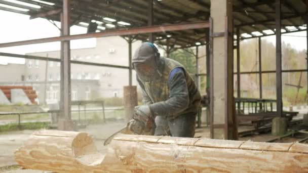 El hombre corta la motosierra de madera para el futuro hogar. Mascarilla protectora en la cara del constructor y mucho aserrín. Hangar con una parte de la futura casa en el fondo — Vídeos de Stock