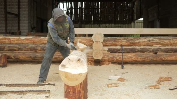 Byggnadsarbetare skär en skåra i trädet för en framtida hem. Skyddande mask och hörlurar på huvudet av byggaren. Hangar med en del av den framtida hem i bakgrunden — Stockvideo