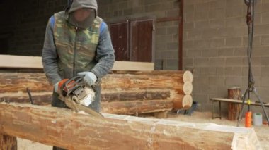 Adam ahşap testere gelecekteki ev için keser. Builder ve bir sürü talaş yüzünde koruyucu yüz maskesi. Hangar gelecekteki ev arka planda bir bölümüyle