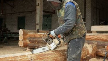 Adam ahşap testere gelecekteki ev için keser. Builder ve bir sürü talaş yüzünde koruyucu yüz maskesi. Hangar gelecekteki ev arka planda bir bölümüyle