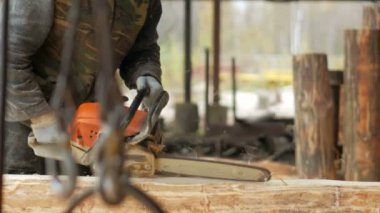 Adam ahşap testere gelecekteki ev için keser. Builder ve bir sürü talaş yüzünde koruyucu yüz maskesi. Hangar gelecekteki ev arka planda bir bölümüyle