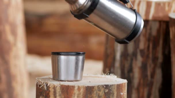 Builder maakt koffiepauze uit een thermos. Houten gebouwen in de achtergrond — Stockvideo