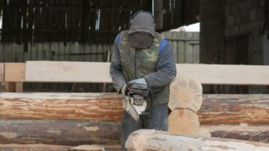 Adam ahşap testere gelecekteki ev için keser. Builder ve bir sürü talaş yüzünde koruyucu yüz maskesi. Hangar gelecekteki ev arka planda bir bölümüyle