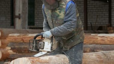 Adam ahşap testere gelecekteki ev için keser. Builder ve bir sürü talaş yüzünde koruyucu yüz maskesi. Hangar gelecekteki ev arka planda bir bölümüyle