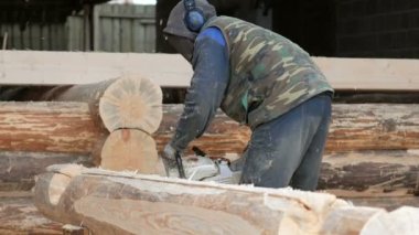 İnşaat işçisi için gelecekteki ev ahşap testere keser. Koruyucu maske ve kulaklık builder ve bir sürü talaş kafasına. Hangar gelecekteki ev arka planda bir bölümüyle