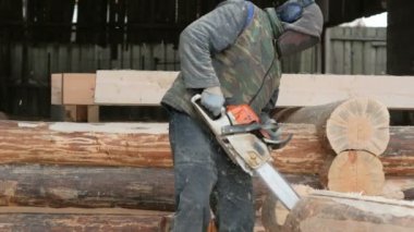 İnşaat işçisi için gelecekteki ev ahşap testere keser. Koruyucu maske ve kulaklık builder ve bir sürü talaş kafasına. Hangar gelecekteki ev arka planda bir bölümüyle