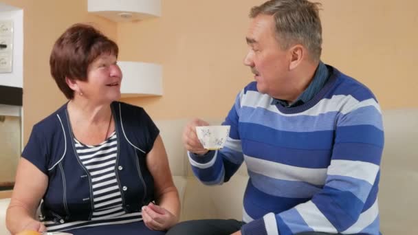 Feliz hombre y mujer mayores hablando en casa con una taza de café. Marido y esposa en una hermosa casa para discutir los eventos del día — Vídeos de Stock