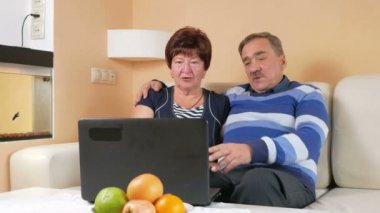Mutlu kıdemli erkek ve bir kadın laptop film izlerken. Sarılmak ve ekranda ne olduğunu tartışmak. Evin güzel iç