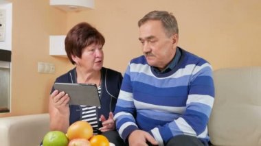 Yaşlı çift doktor Danışma tablet Pcs. Man öksürük için alır ve doktor tavsiye internette verir. Karı koca güzel bir evde kanepede oturan