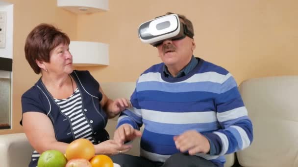 Homem sênior colocando óculos pela primeira vez realidade virtual junto com uma mulher. O homem balança os braços e balança a cabeça. A esposa segura a mão de seus maridos e olhando com cuidado . — Vídeo de Stock