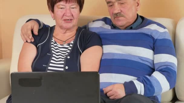 Ευτυχής ανώτερος άνθρωπος και μια γυναίκα βλέποντας μια ταινία για το φορητό υπολογιστή. Αυτοί αγκαλιάζουν και να συζητήσουν τι συμβαίνει στην οθόνη. Όμορφο εσωτερικό του σπιτιού — Αρχείο Βίντεο