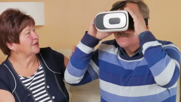 Senior man putting on glasses for the first time virtual reality together with a woman. The man swings his arms and shakes his head. The wife holds her husbands hand and looking carefully. — Stock Video